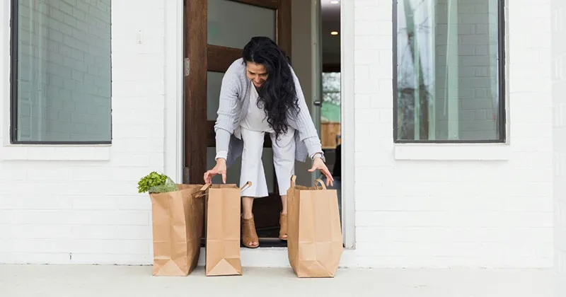 woman picking up heavy grocery bags from front porch